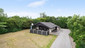 A small, single-story building with a covered patio area, surrounded by dense greenery.