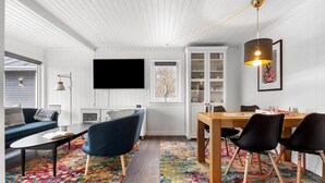 Ein modernes Wohnzimmer mit einer Couch, einem Couchtisch, einem Fernseher und einem Essbereich mit Stühlen und einem Tisch.