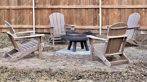 Un jardin avec une clôture en bois, une table ronde et quatre chaises Adirondack.