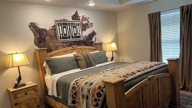 Un lit en bois recouvert d’une couverture à motifs, deux lampes de chevet, une table de chevet et un élément décoratif mural.
