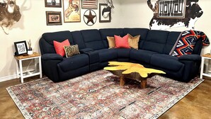 Un salon avec un canapé d’angle bleu foncé, un tapis à motifs et divers éléments de décoration murale, notamment des motifs animaliers et la silhouette d’une vache.