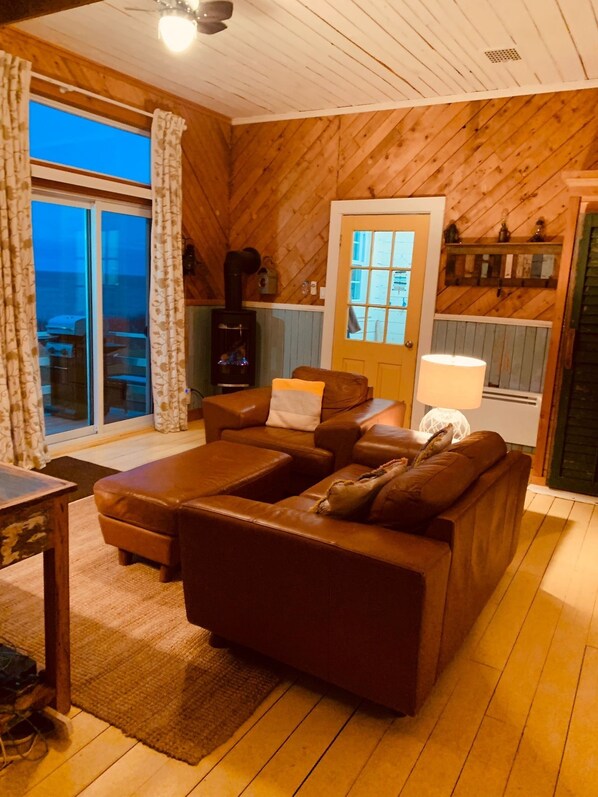Un salon chaleureux avec un canapé en cuir marron, un plancher en bois et une grande fenêtre agrémentée de rideaux.