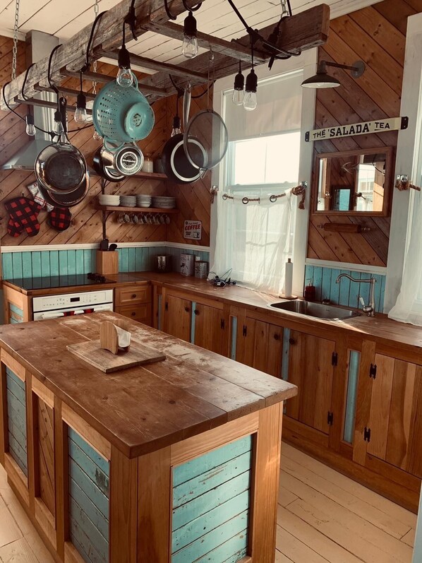 A rustic kitchen with wooden cabinets, a central island, hanging pots, and a sign for 'The Salada Tea'. - Breathtaking ocean views, peace, and relaxation (Gaspé)