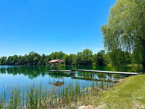 Un lago tranquilo con un muelle, orillas cubiertas de hierba y una estructura de techo rojo al fondo.