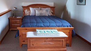 A bedroom with a wooden bed, a nightstand, a bedside table, a bench, and a wall-mounted picture. - Cozy lakefront cabin on Big Beaver Lake (Big Lake)