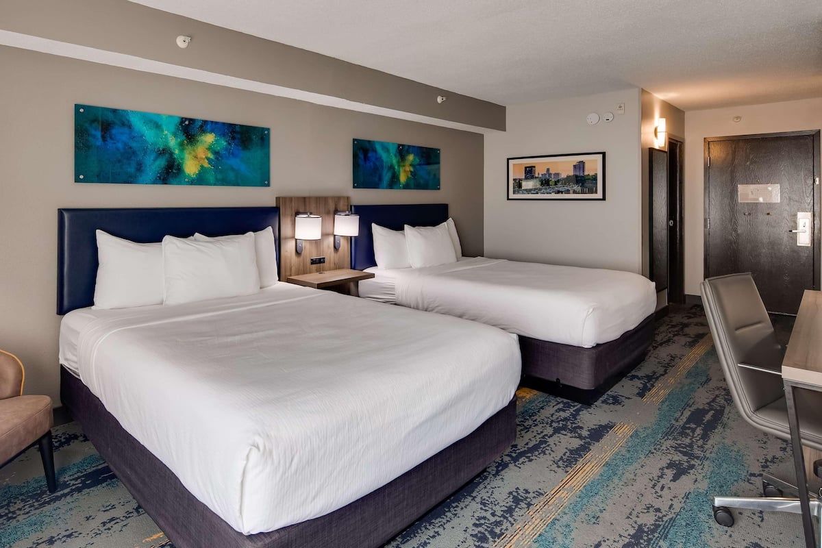 A hotel room with two beds, a desk, a chair, and artwork on the walls.