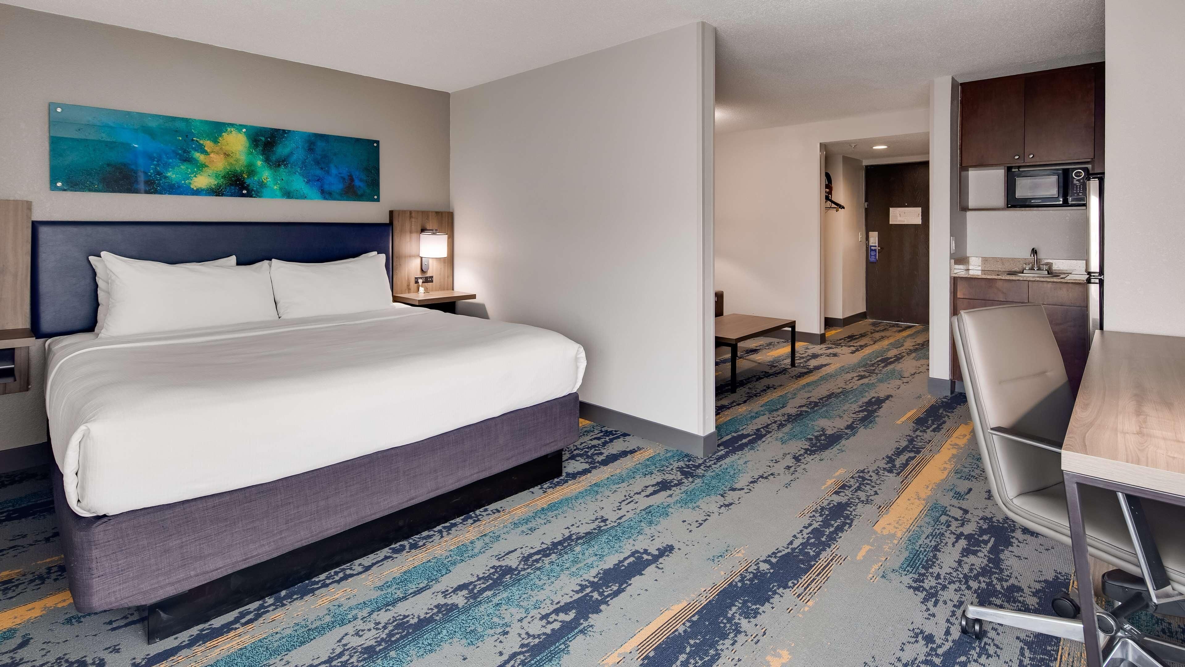 A hotel room with a large bed, a desk, a chair, a microwave, and a painting on the wall.