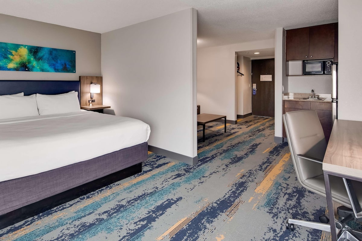 A hotel room with a large bed, a desk, a chair, a microwave, and a painting on the wall.