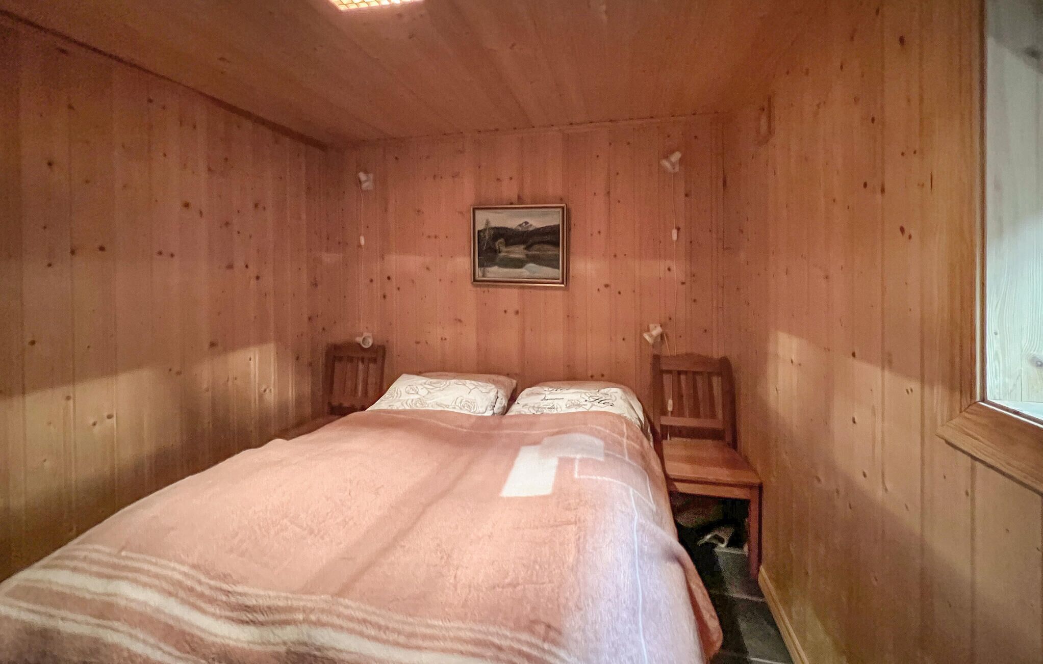 Una stanza in legno con un letto, due sedie, un quadro appeso al muro e una finestra.