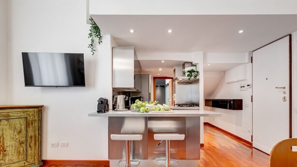A modern kitchen with a central island, two bar stools, a flat-screen TV, and a wooden floor.