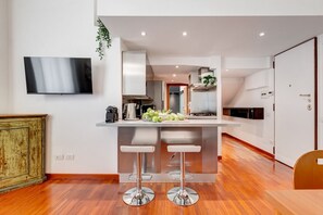 Een moderne keuken met een centraal eiland, twee barkrukken, een flatscreen televisie en een houten vloer.