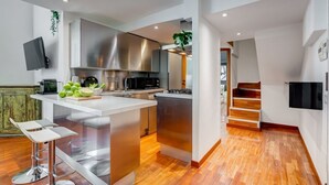 A modern kitchen with stainless steel appliances, a central island, and a wooden staircase.