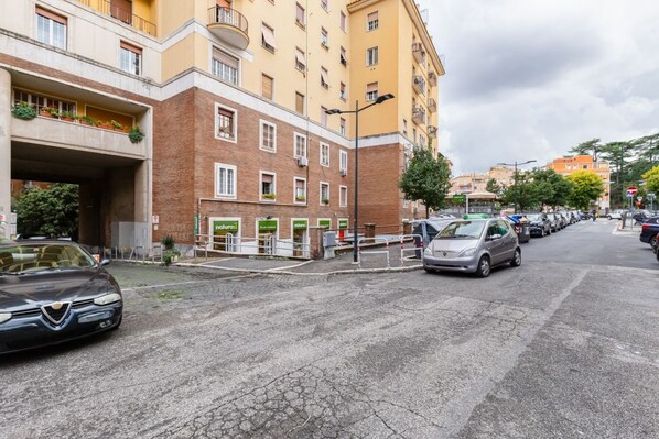 A multi-story building with a brick facade, a covered parking area, and a row of parked cars.