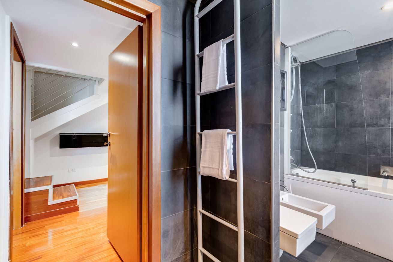 A modern bathroom with dark tiles, a shower, a white sink, and a towel rack.