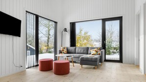 A modern living room with a grey sofa, two red ottomans, a small round table, and a TV mounted on the wall.