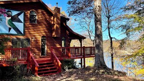 A log cabin with a red staircase leading to a deck, surrounded by trees and a lake. - Secluded lakeside retreat with lake view and hot tub. Close to Mammoth Cave.  (Cub Run)