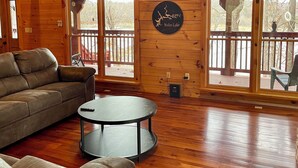 A spacious wooden cabin interior with a large sofa, a round coffee table, and a sign reading "Nolin Lake". - Secluded lakeside retreat with lake view and hot tub. Close to Mammoth Cave.  (Cub Run)
