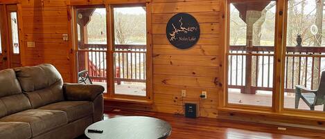 A spacious wooden cabin interior with a large sofa, a round coffee table, and a sign reading "Nolin Lake".