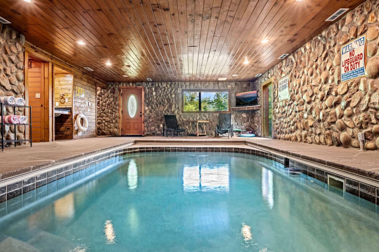 A pool area with a stone wall, wooden ceiling, and a lifeguard duty sign.