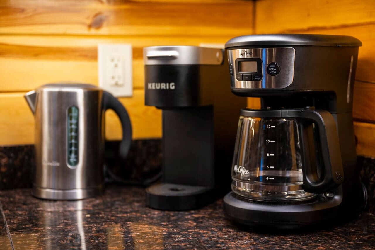 Une machine à café, une machine à capsules Keurig et une bouilloire en acier inoxydable sur un plan de travail de cuisine.