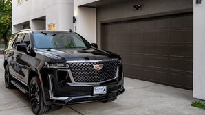 A black Cadillac SUV parked in front of a modern building with a garage. - Designer Luxury for 10•Rooftop Deck•Rice Military (HOUSTON)