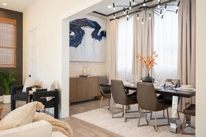 A modern dining area with a table set for four, a large abstract painting on the wall, and a potted plant.