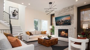 A modern living room with a staircase, a fireplace, and a cityscape painting. - Premium House for 10 w/ Rooftop Deck in Rice Mil (HOUSTON)