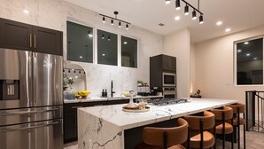 A modern kitchen with a marble island, stainless steel appliances, and a seating area with leather chairs. - Premium House for 10 w/ Rooftop Deck in Rice Mil (HOUSTON)