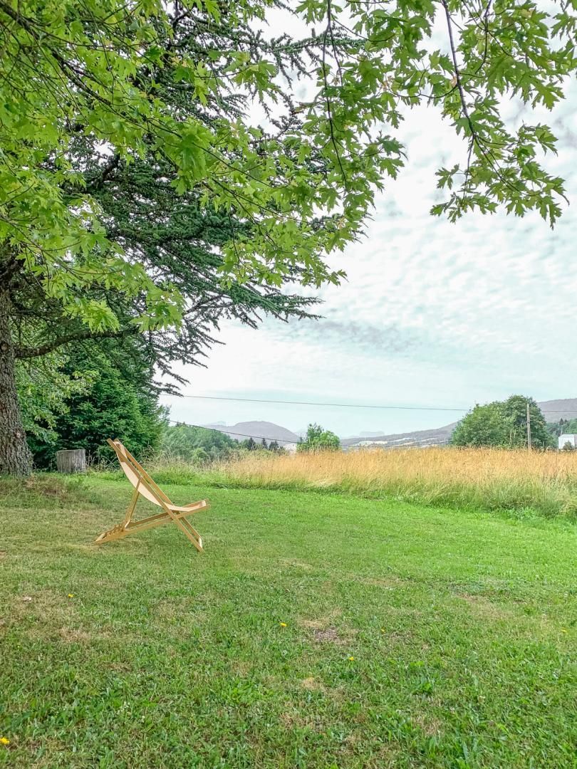 A grassy outdoor area with a wooden swing set and a large tree providing shade.