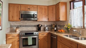 Une cuisine avec des meubles en bois, des appareils électroménagers en acier inoxydable, un pare-feu en carrelage et une fenêtre avec un rideau.
