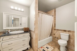 Bathroom features a large vanity, bathtub, and toilet, with a mirror above the vanity and a patterned rug on the floor.