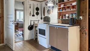 A compact kitchen with a white stove, a wooden cabinet, and a shelf with kitchenware.