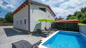 A modern house with a swimming pool, a patio with lounge chairs, and a green umbrella. - Cozy apartment in Peroj with WiFi (Peroj)