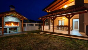 A backyard with a stone fireplace, a covered patio with a table and chairs, and a well-maintained lawn. - Cozy apartment in Peroj with WiFi (Peroj)