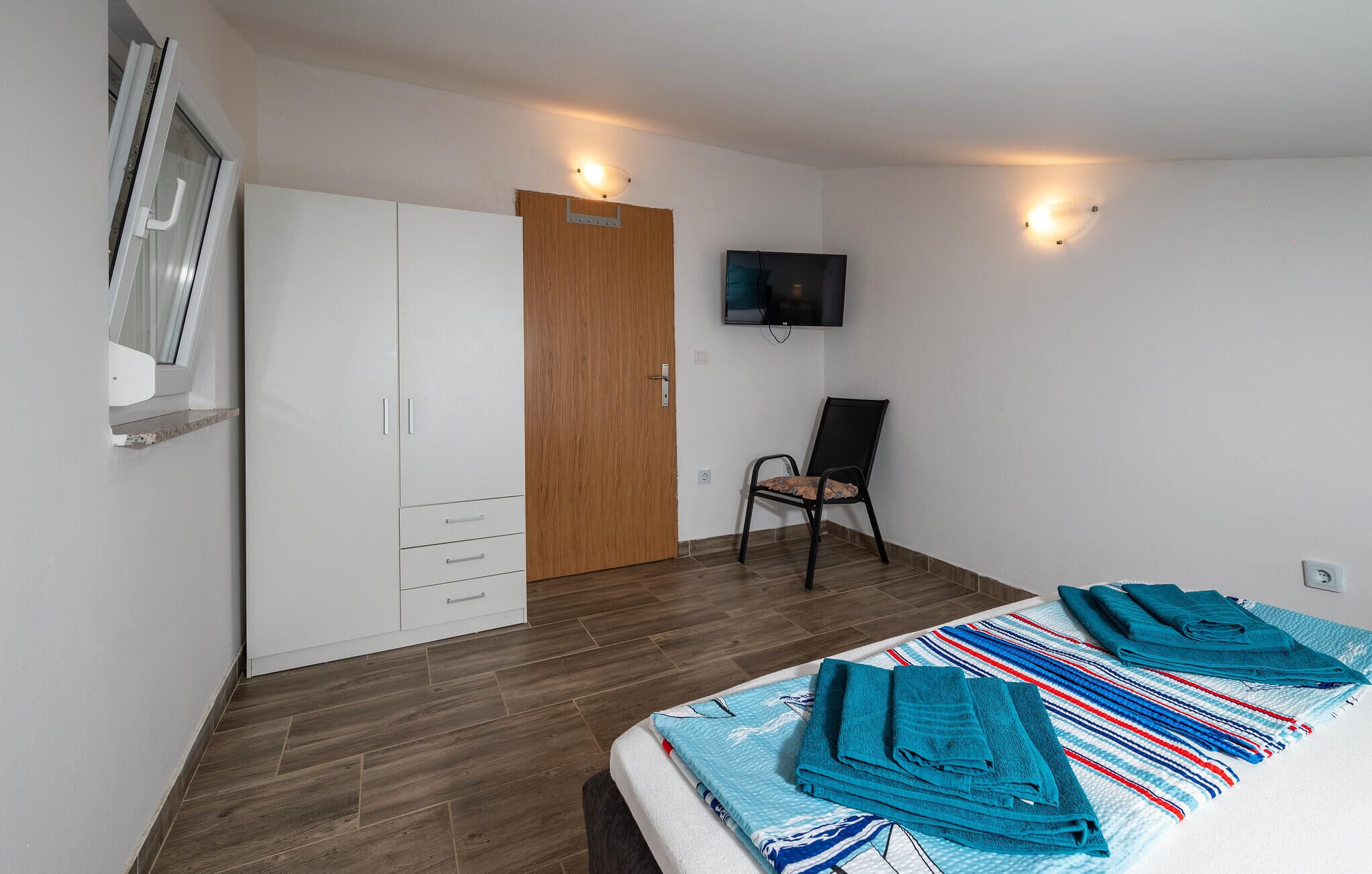 A bedroom with a bed, a wooden wardrobe, a television, and a chair.