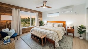 A modern bedroom with a large bed, wooden panel walls, a ceiling fan, and a view of the outdoors. - Bryce Zion Vacation (Kane County)