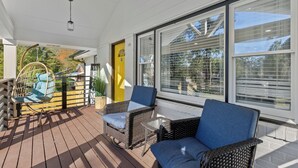 A covered outdoor seating area with wicker furniture and a swing chair, large windows, and a yellow door. - Cozy Decatur Home with Indoor Fireplace & Firepit (Decatur)