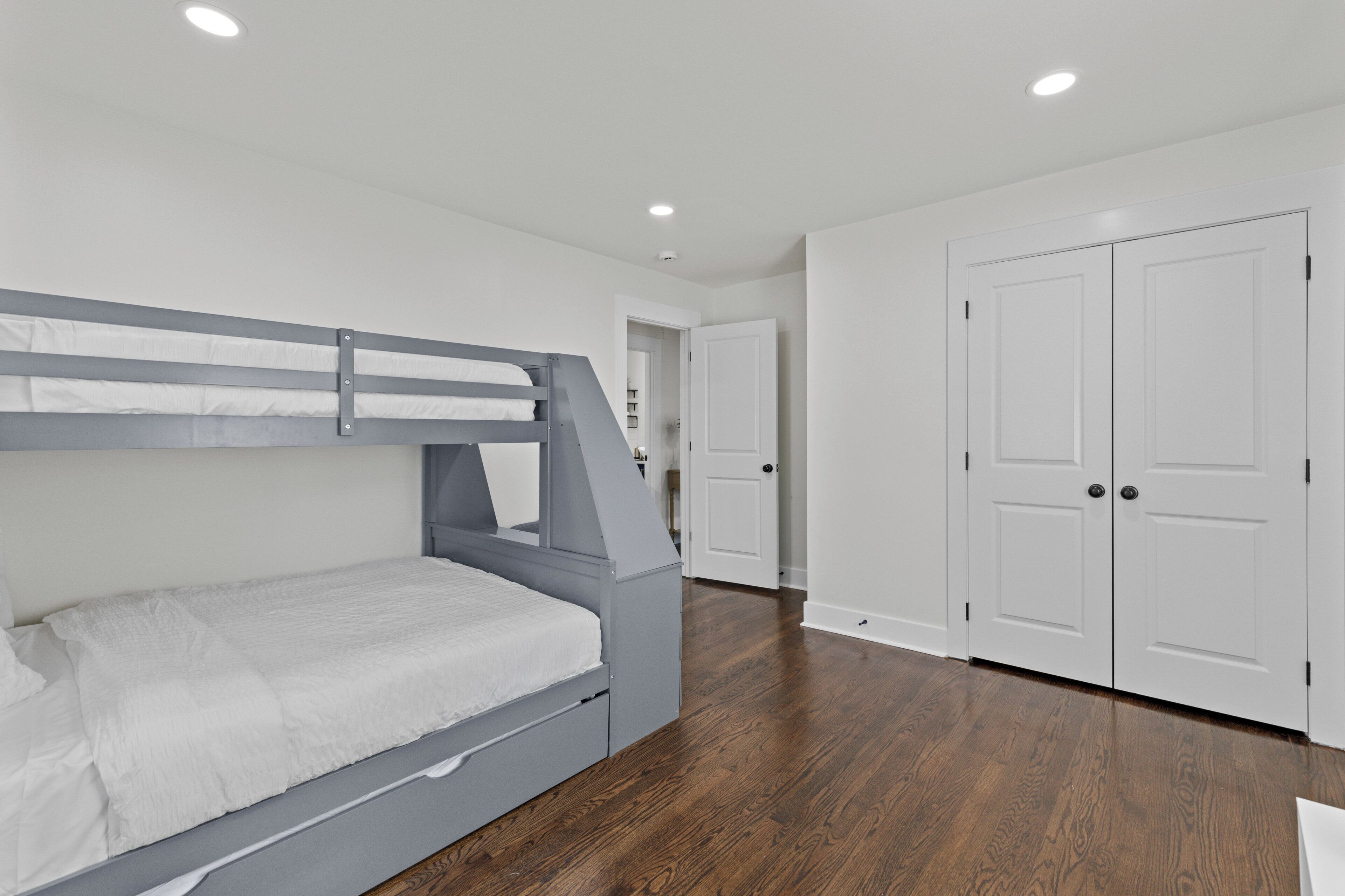 Ein Schlafzimmer mit Etagenbett, weißen Wänden, Holzboden und einem weißen Kleiderschrank.