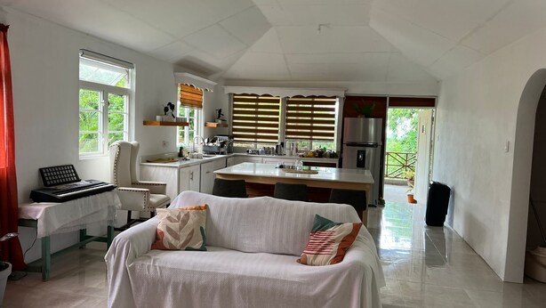 A spacious living area with a sofa, a small table, and a keyboard. There is a kitchen area with a refrigerator and a sink. - Modern Eco lodge with A/C in bedrooms and 40ft patio for relaxation and fun. (St. Sylvans Village)
