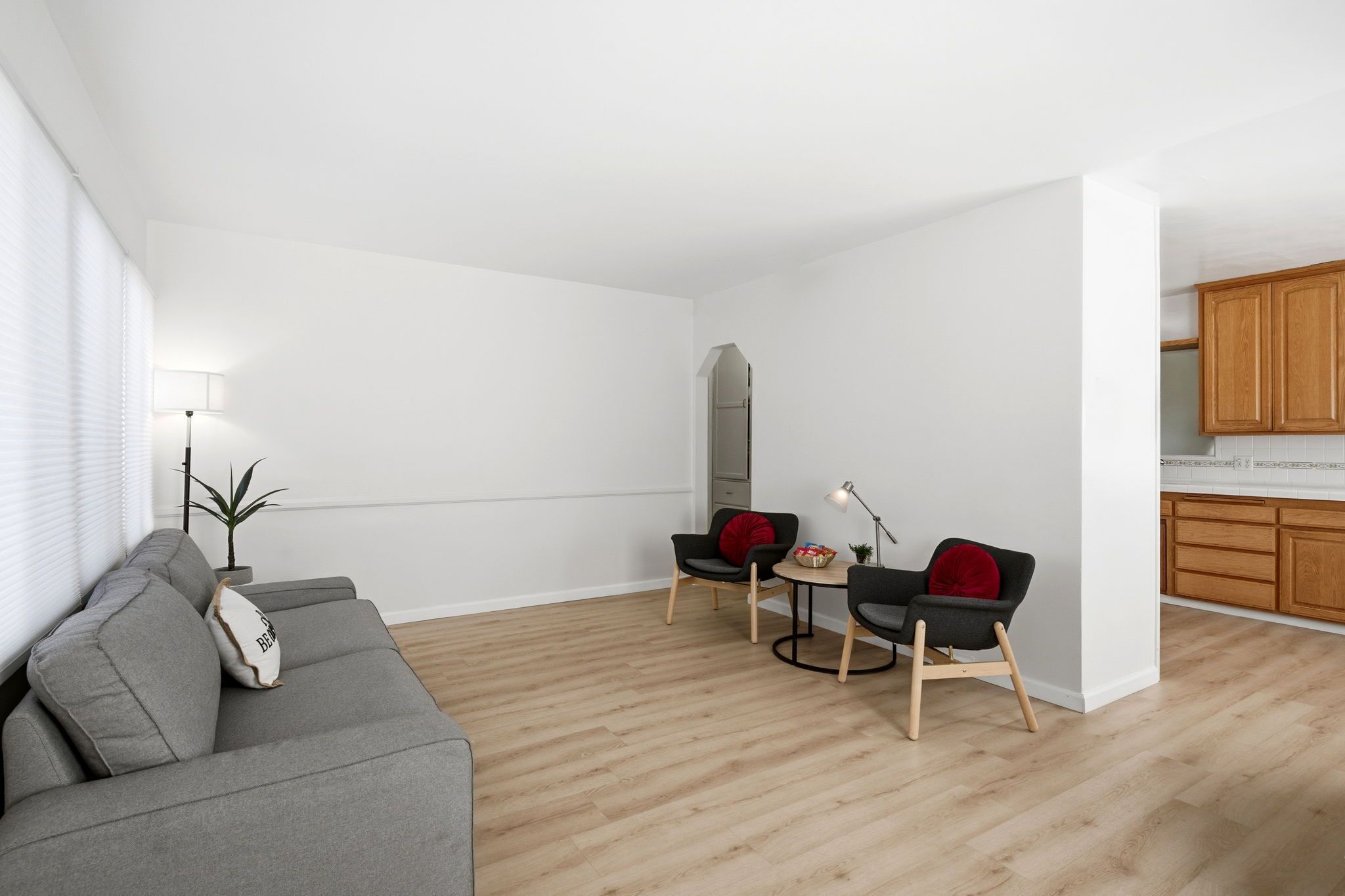 Una sala de estar moderna con un sofá gris, dos sillas negras, una mesita y una lámpara. En el fondo, hay un aparador de madera.