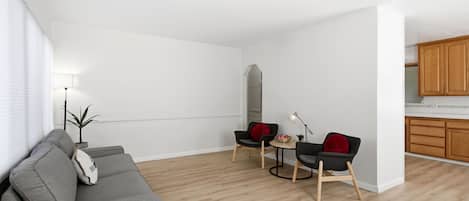 Una sala de estar moderna con un sofá gris, dos sillas negras, una mesita y una lámpara. En el fondo, hay un aparador de madera.