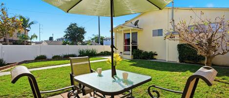 A patio with a table and chairs, a green umbrella, and a house in the background.