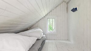 Une petite pièce en bois, peinte en blanc, avec un lit simple et une fenêtre.