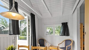 Une pièce avec une table blanche, deux chaises en bois, une plante en pot et une lampe suspendue.