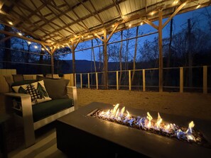 An outdoor patio with a fire pit, a cushioned seating area, and a wooden fence. - Creekside Mountain Cabin Getaway - 6 Acres, Mountain Views, Hot Tub (Cosby)