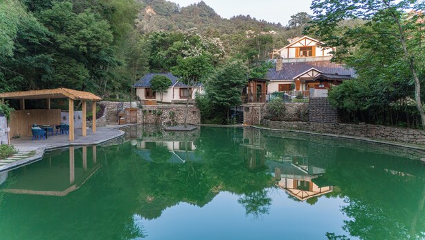 A serene pool area with a wooden deck, stone walls, and traditional-style buildings in the background. - ZhangJiaJieFuXiErYi (Zhangjiajie)