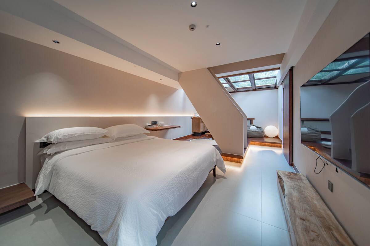 A modern bedroom with a large bed, a wooden bench, and a skylight.