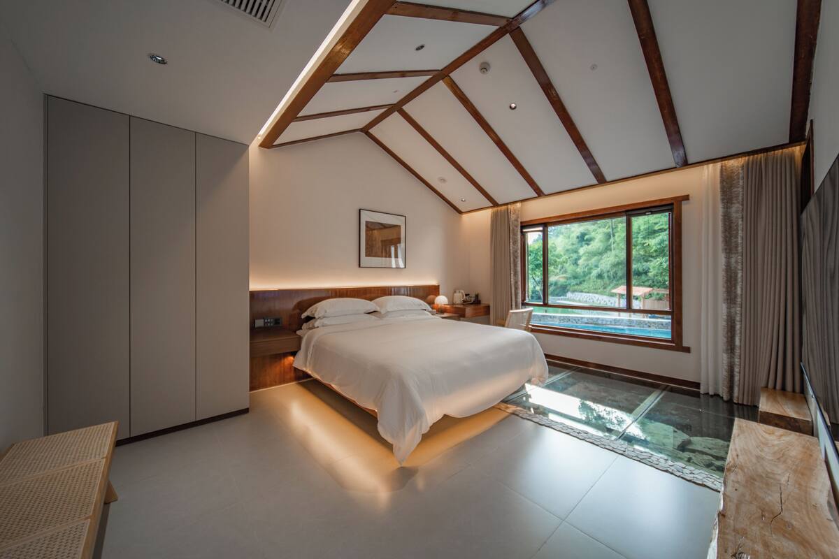 A modern bedroom with a large bed, built-in wardrobe, and a view of a swimming pool.