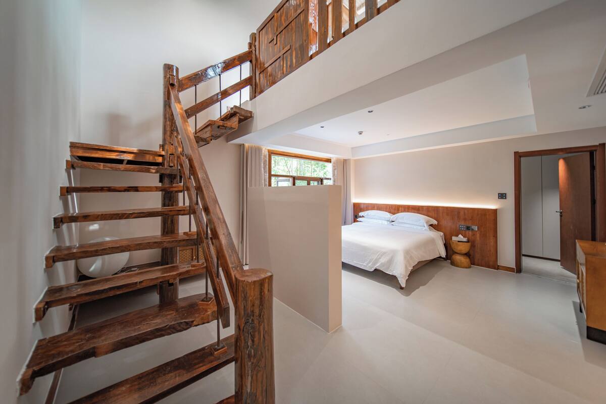 A modern bedroom with a wooden staircase, a large bed, and a nightstand.