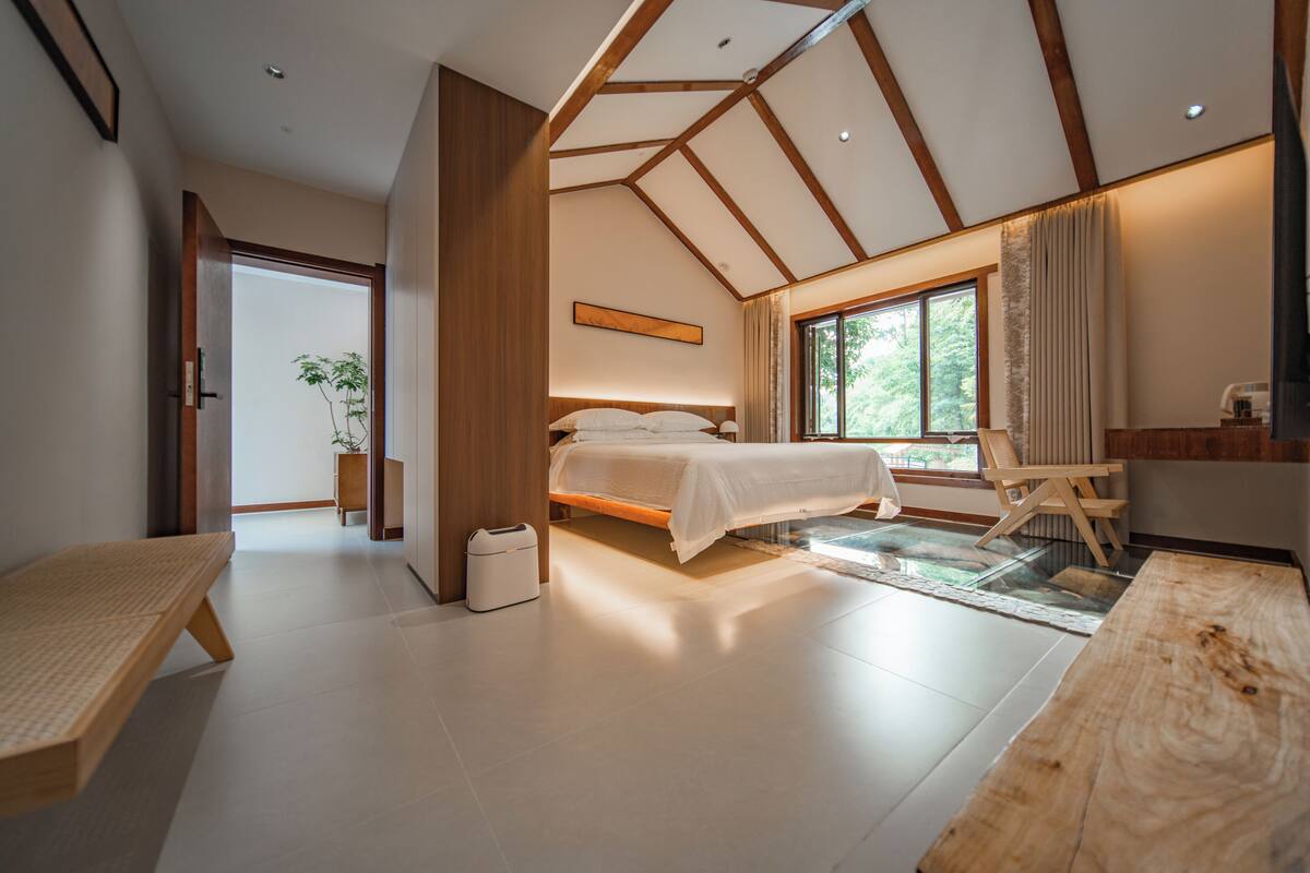 A modern bedroom with a large bed, a wooden bench, and a glass table.